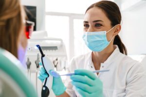 水色のマスクをした歯科医が治療器具を持ち患者の口内を診察しようとしている