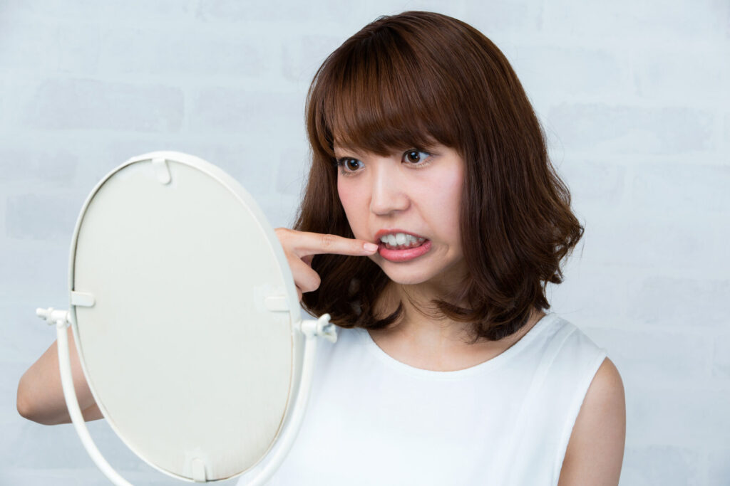 セミロングヘアの女性が鏡を見て口元を指している