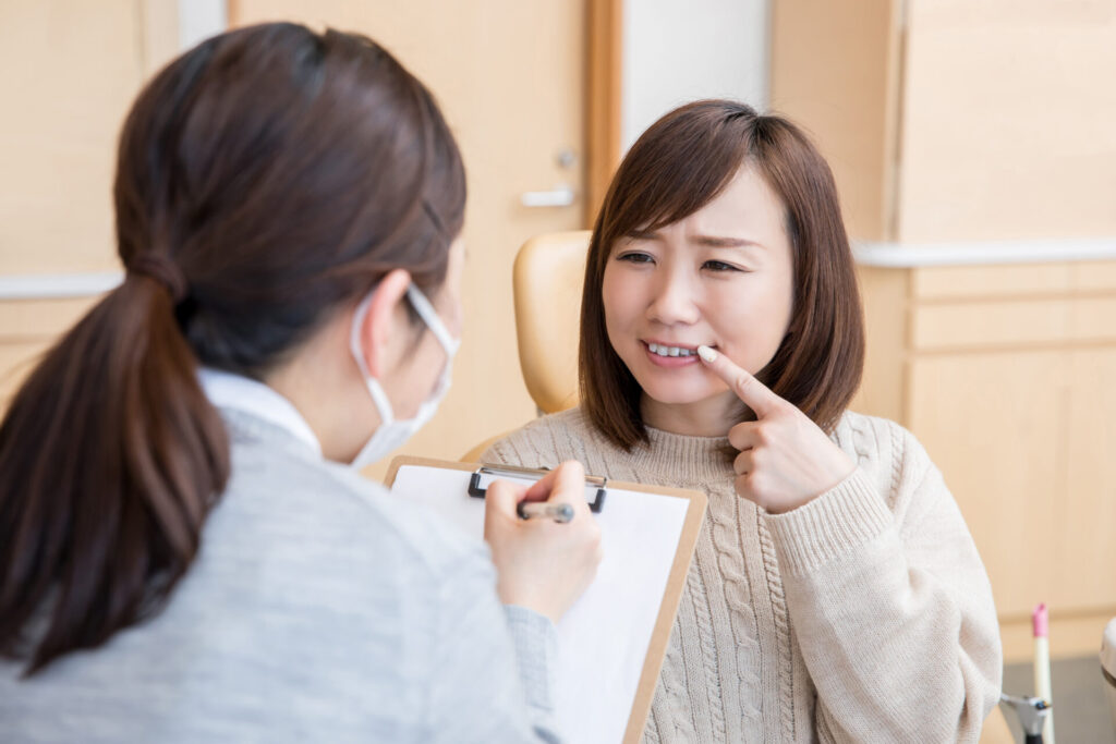 歯を指差し歯科医院で相談している女性